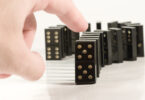 Human hand ready to push a row of black dominoes.