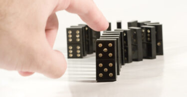 Human hand ready to push a row of black dominoes.