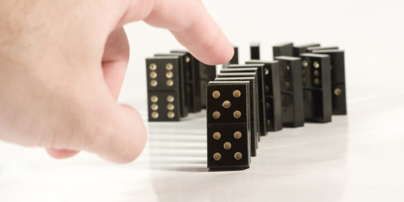 Human hand ready to push a row of black dominoes.