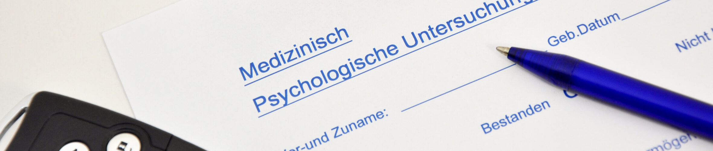 Oberer Teil eines Medizinisch-psychologischen Gutachtens. Darauf liegen ein Autoschlüssel und ein Stift. Darunter liegt, halb verdeckt, ein Führerschein.