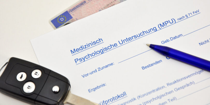 Oberer Teil eines Medizinisch-psychologischen Gutachtens. Darauf liegen ein Autoschlüssel und ein Stift. Darunter liegt, halb verdeckt, ein Führerschein.