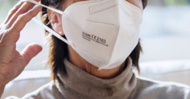 Nahaufnahme der Mund-Nasen-Partie einer Frau, die gerade eine FFP-2-Maske aufzieht.