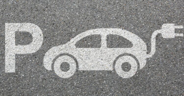 Zeichnung auf Asphalt, bestehend aus einem großen P für "Parkplatz" sowie der schematischen Darstellung eines Elektrofahrzeugs.