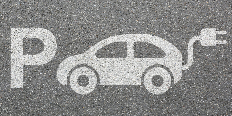 Zeichnung auf Asphalt, bestehend aus einem großen P für "Parkplatz" sowie der schematischen Darstellung eines Elektrofahrzeugs.