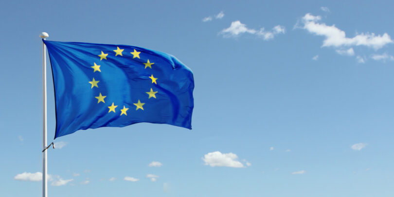 EU flag waving against blue sky with clouds.