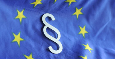 Paragrafenzeichen vor dem Hintergrund der Flagge der Europäischen Union.