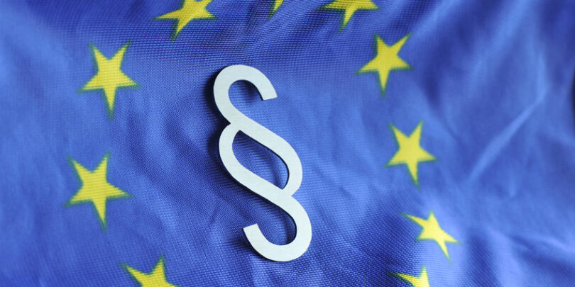 Paragrafenzeichen vor dem Hintergrund der Flagge der Europäischen Union.
