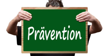 Mann, der eine grüne Tafel vor sich hält, auf der in weißer Schrift Prävention geschrieben steht.