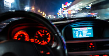 Verschwommene Perspektive auf das Armaturenbrett eines Autos und die Straße hinter der Windschutzscheibe.