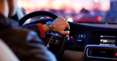 Nahaufnahme des Lenkrads eines Autos und der es steuernden Hand des Fahrers.