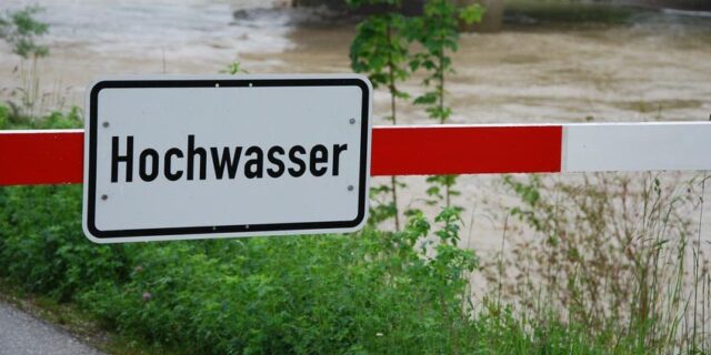 Heruntergelassene Schranke, an der ein Schild mit der Aufschrift Hochwasser angebracht ist.