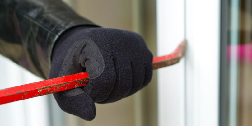 Burglar wearing black clothes and leather coat breaking in a house.
