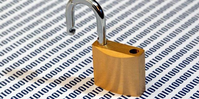 Gehöffnetes Vorhängeschloss auf einer Unterlage, die Nullen und Einsen zeigt.