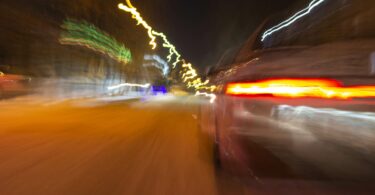 The car is driving at high speed on the night street of the city. Blurred image along the lines of the road with zoom.