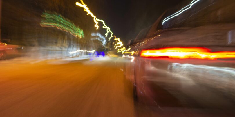 The car is driving at high speed on the night street of the city. Blurred image along the lines of the road with zoom.