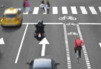 Blurred cars, bikes and pedestrians on busy street.