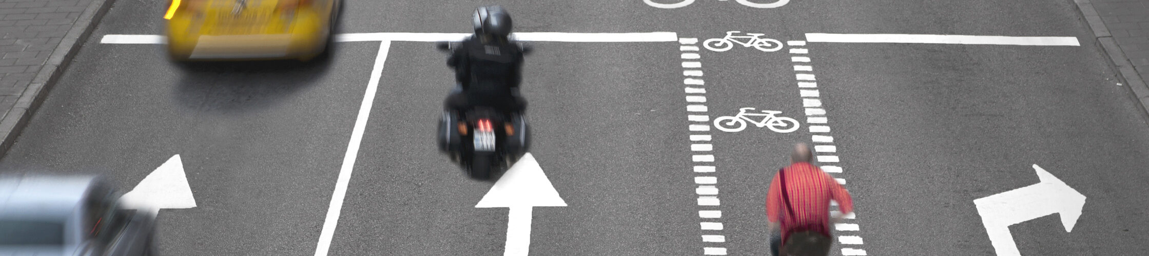 Blurred cars, bikes and pedestrians on busy street.