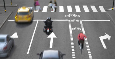 Blurred cars, bikes and pedestrians on busy street.