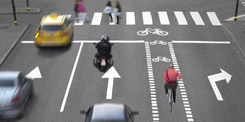 Blurred cars, bikes and pedestrians on busy street.