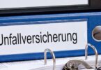 Blauer Aktenordner, der auf einem Schreibtisch liegt und auf dessen Rückenschild "Unfallversicherung" steht.