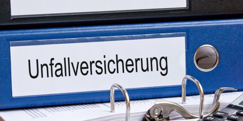 Blauer Aktenordner, der auf einem Schreibtisch liegt und auf dessen Rückenschild "Unfallversicherung" steht.