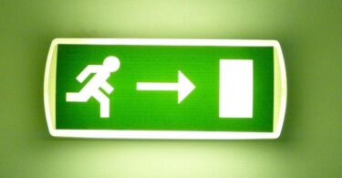 Grün leuchtendes Fluchtwegschild vor grünem Hintergrund.