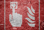 Weißes Graffiti eines Brandschutzzeichens auf einer roten Ziegelsteinmauer.