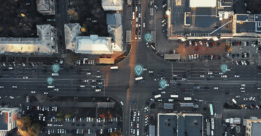 Aerial view of city intersection with many cars and GPS navigation system symbols. Autonomous driverless vehicles in city traffic.