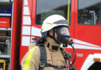 Feuerwehrmann mit Gasmaske vor geöffnetem Feuerwehrwagen.