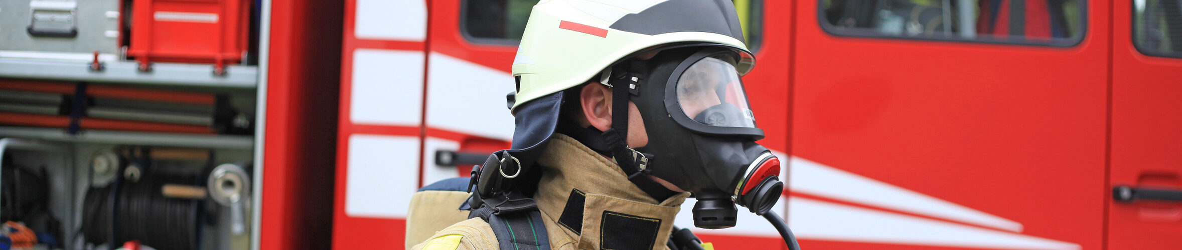 Feuerwehrmann mit Gasmaske vor geöffnetem Feuerwehrwagen.
