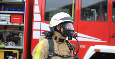 Feuerwehrmann mit Gasmaske vor geöffnetem Feuerwehrwagen.