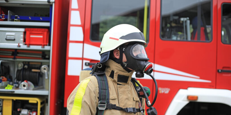 Feuerwehrmann mit Gasmaske vor geöffnetem Feuerwehrwagen.