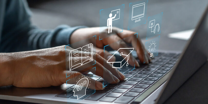 Nahaufnahme zweier Hände, die die Tastatur eines geöffneten Laptops bedienen. Über den Händen schweben folgende virtuelle Symbole: ein Kopf mit Zahnrädern darin, ein aufgeschlagenes Buch, eine Person, die ein Smartbord bedient, ein Doktorhut, ein Bildschirm, ein Headset, eine leuchtende Glühbirne.
