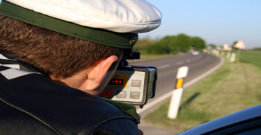 Blick über die Schulter eines deutschen Polizisten, der Geschwindigkeit mit einer Radarpistole auf einer Landstraße misst.
