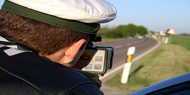 Blick über die Schulter eines deutschen Polizisten, der Geschwindigkeit mit einer Radarpistole auf einer Landstraße misst.